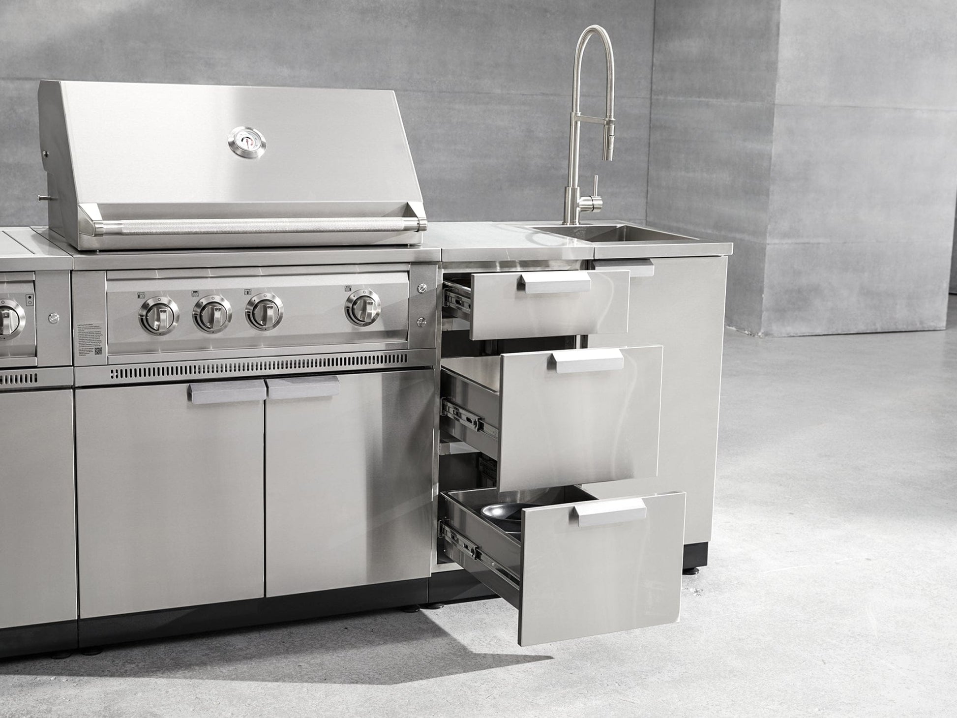Premium stainless steel outdoor kitchen with grill, sink, and storage cabinets on sleek gray concrete flooring.