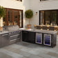 Mont Alpi outdoor kitchen with stainless grill, burners, fridge, counter space, dining table, and lush plants nearby.