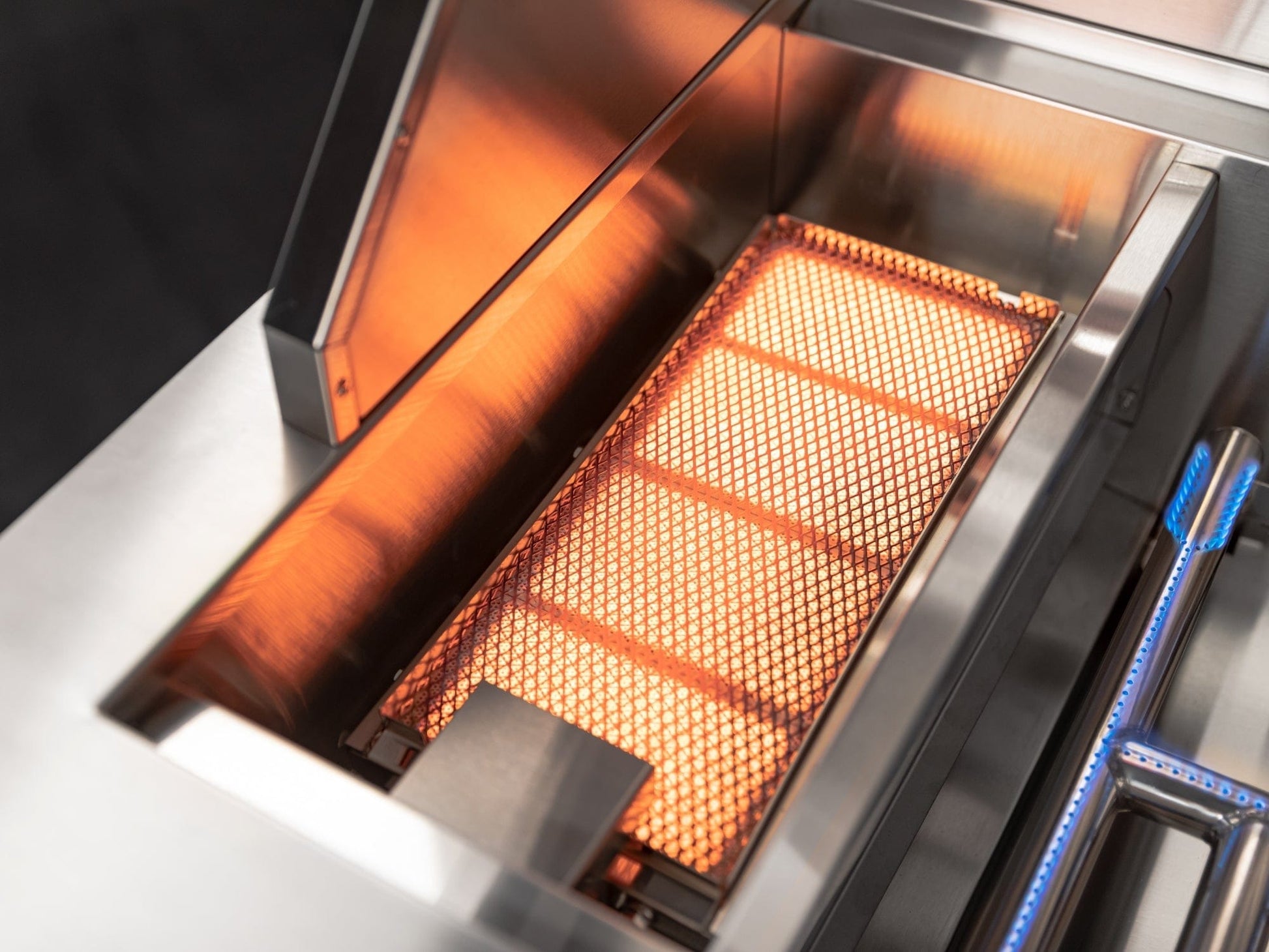 Lit NewAge infrared grill burner in a sleek stainless steel outdoor kitchen setup with premium finish.