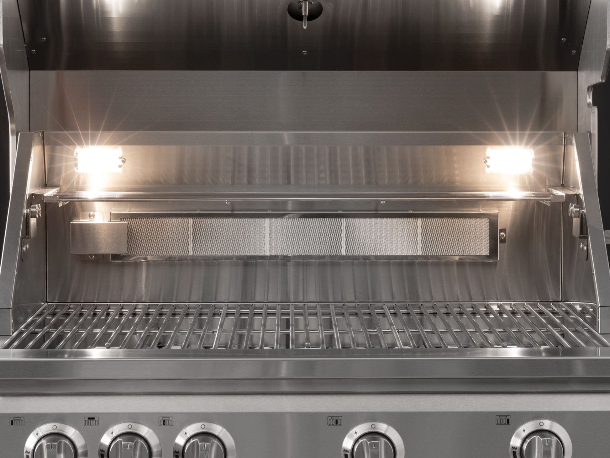NewAge stainless steel gas grill with open lid, illuminated burners, and control knobs in modular outdoor kitchen.
