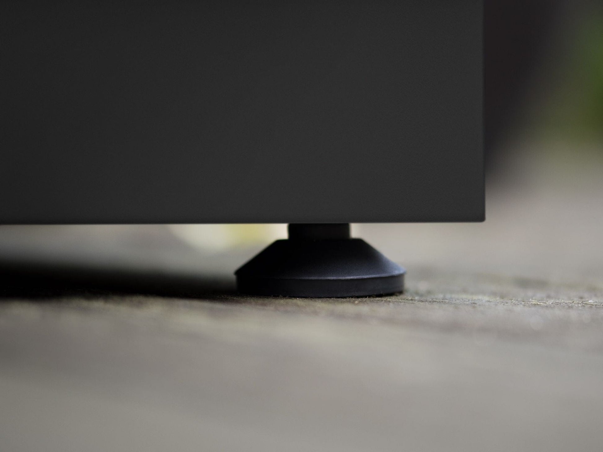 Black rubber foot supports NewAge outdoor kitchen cabinet on wood decking, highlighting quality construction.