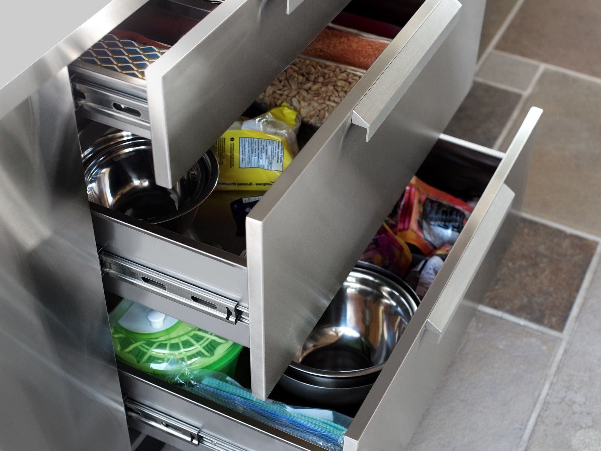 Three open stainless steel cabinets organize pet food, treats, bowls, and cleaning supplies in a sleek outdoor finish.