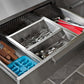 Sleek NewAge steel drawer with organized cutlery, knives, blue ice tray, and red board for premium outdoor kitchens.
