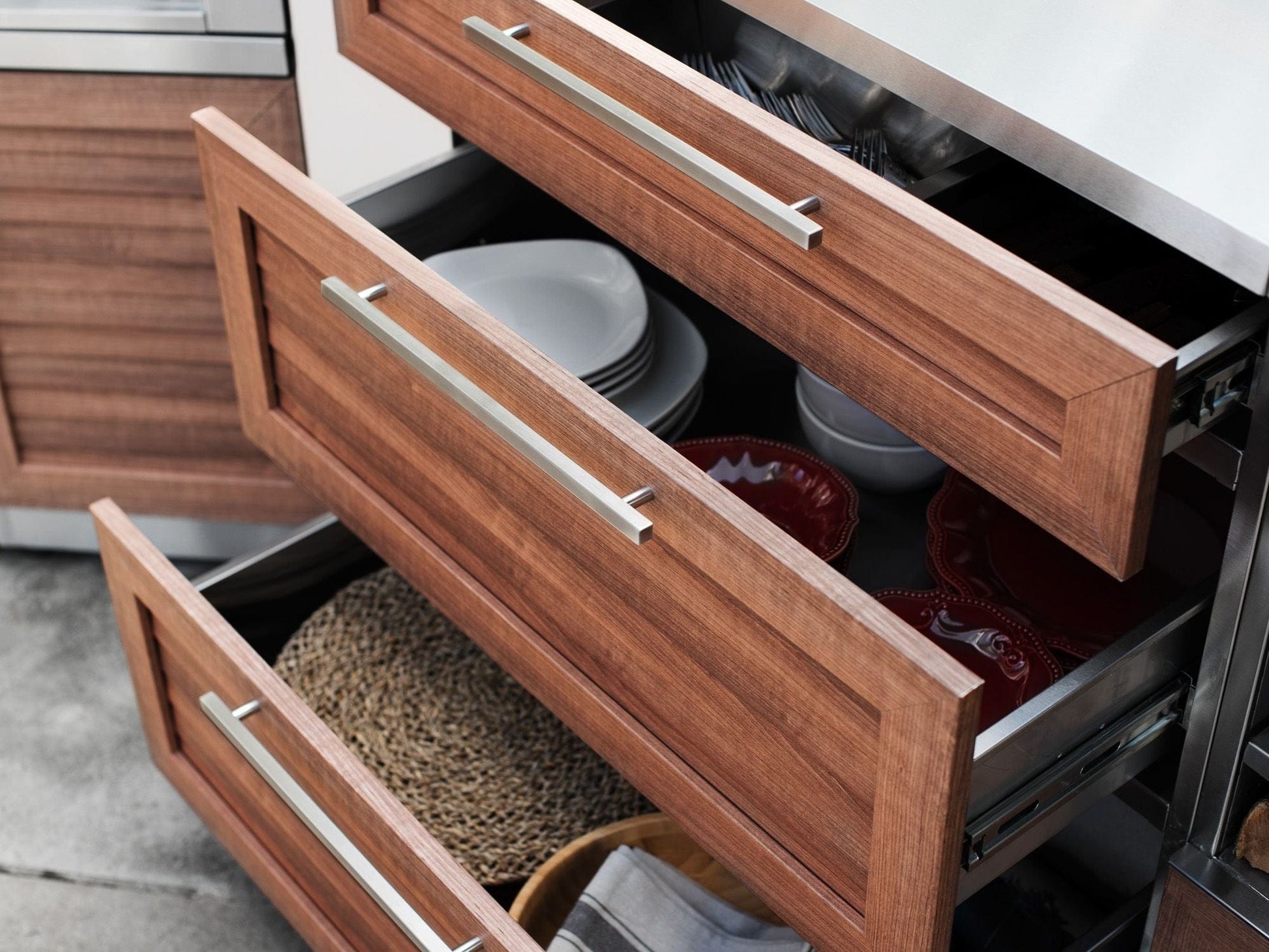 Open kitchen drawers display neatly organized plates, bowls, and placemats for premium outdoor kitchens with sink access.