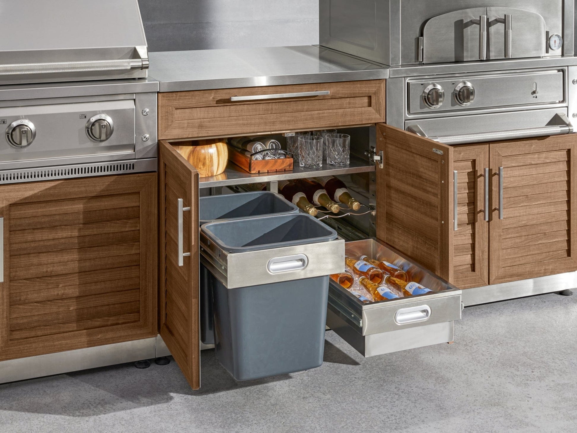 Open wooden outdoor kitchen cabinets with pull-out trash bins, stainless steel grills, and premium outdoor finish.