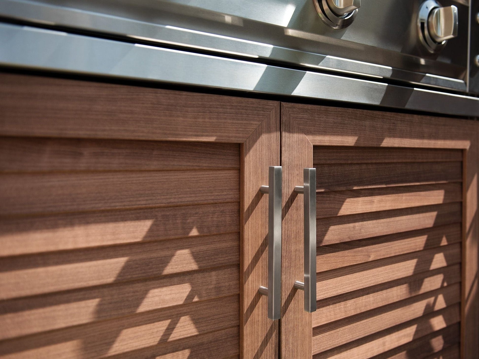 Premium NewAge outdoor kitchen cabinets with brushed metal handles beneath a stainless appliance with control knobs.