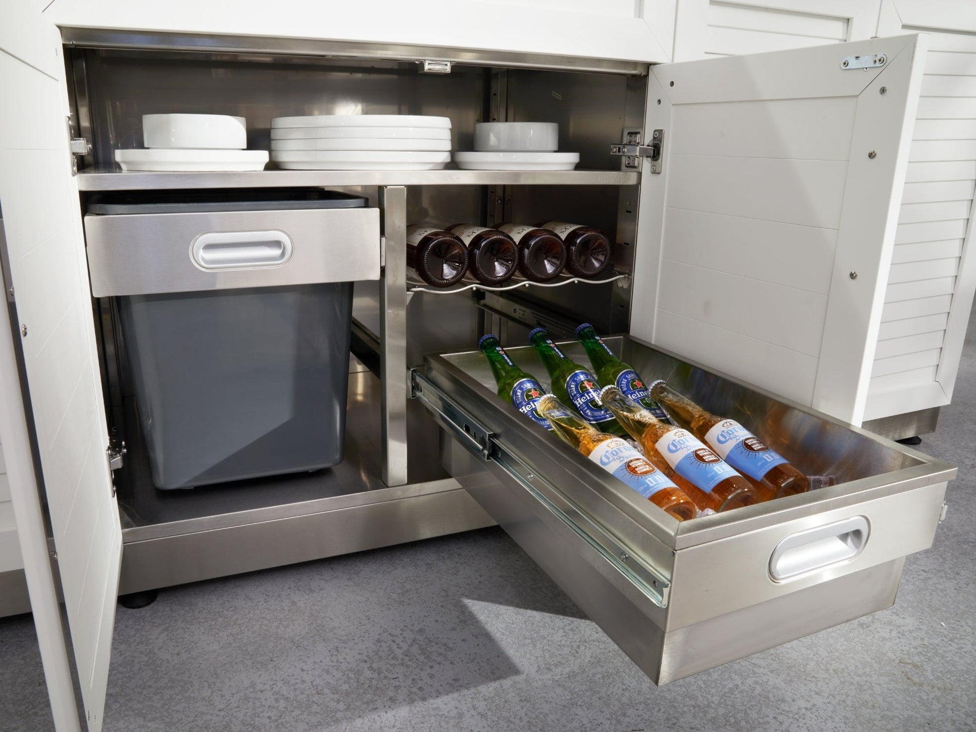 Open NewAge stainless steel cabinet with plates, trash bin, wine bottles, and drawer with bottled drinks.