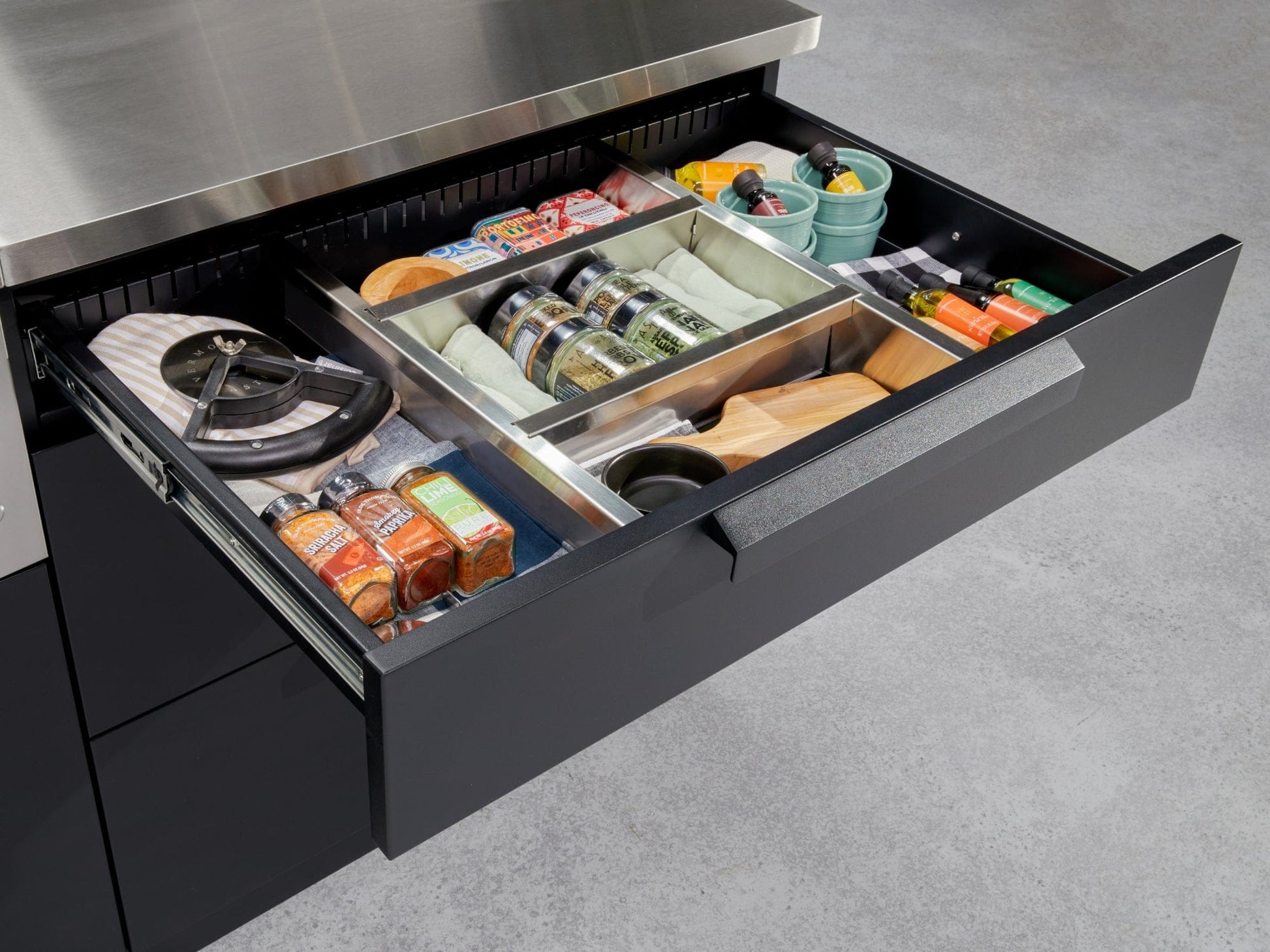 Premium modular outdoor kitchen drawer open, showing organized spices, utensils, and containers in stainless finish.