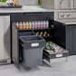 Outdoor kitchen cabinets with open drawers showing drinks, bottles, cans, and two trash bins in a sleek finish.