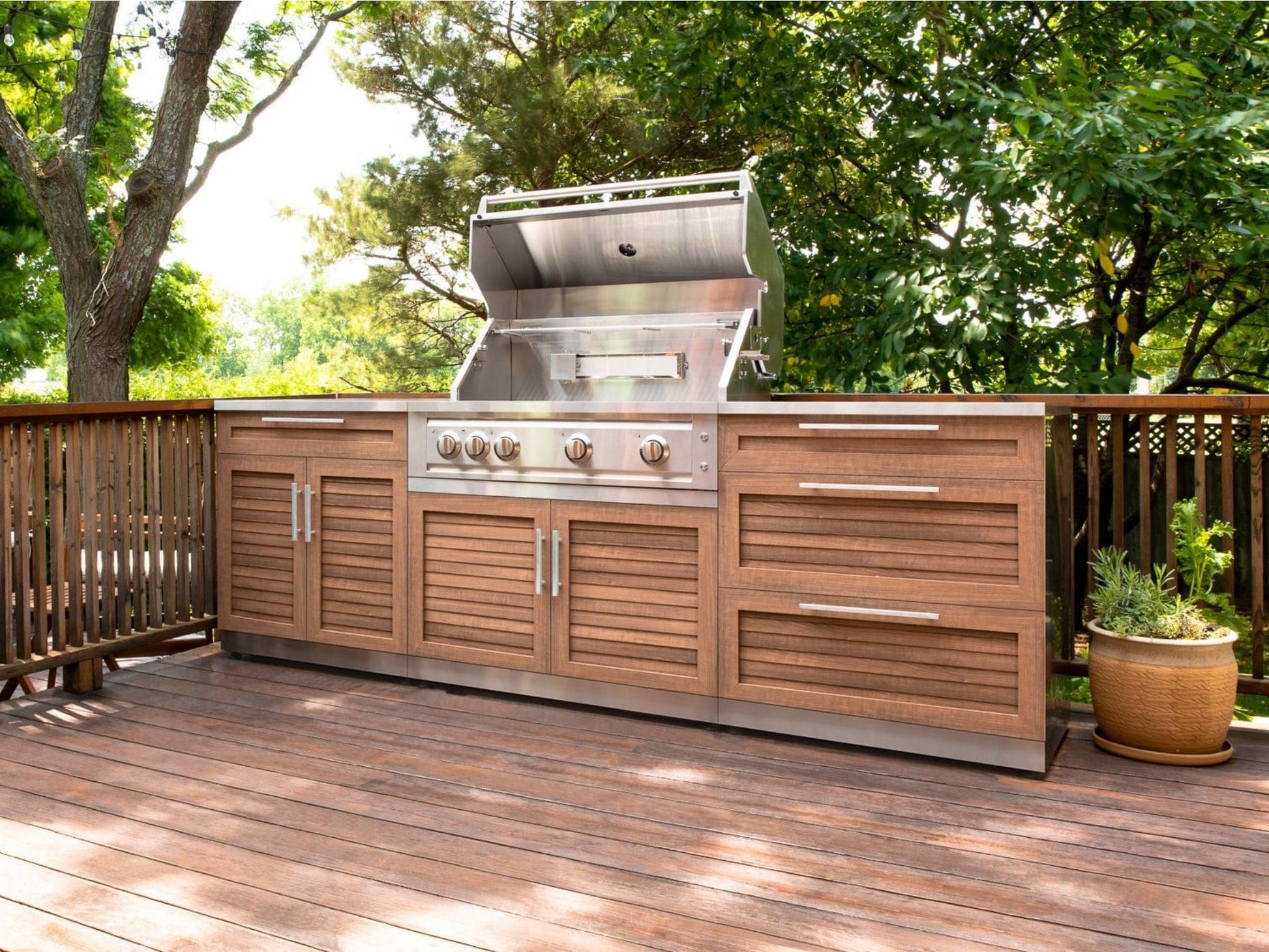 Premium outdoor kitchen with stainless steel grill, modular cabinets, wood deck, and potted plant accents.