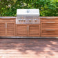 Premium outdoor kitchen grill with modular cabinets, sink, and fridge on wood deck amid lush trees.